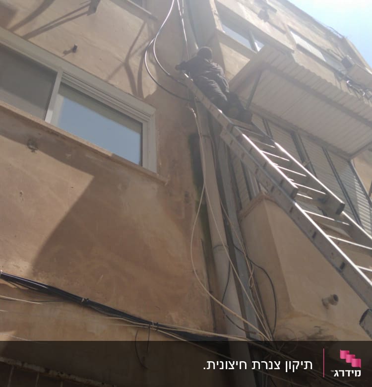 אדם על סולם מתקן צינורות על קיר בניין